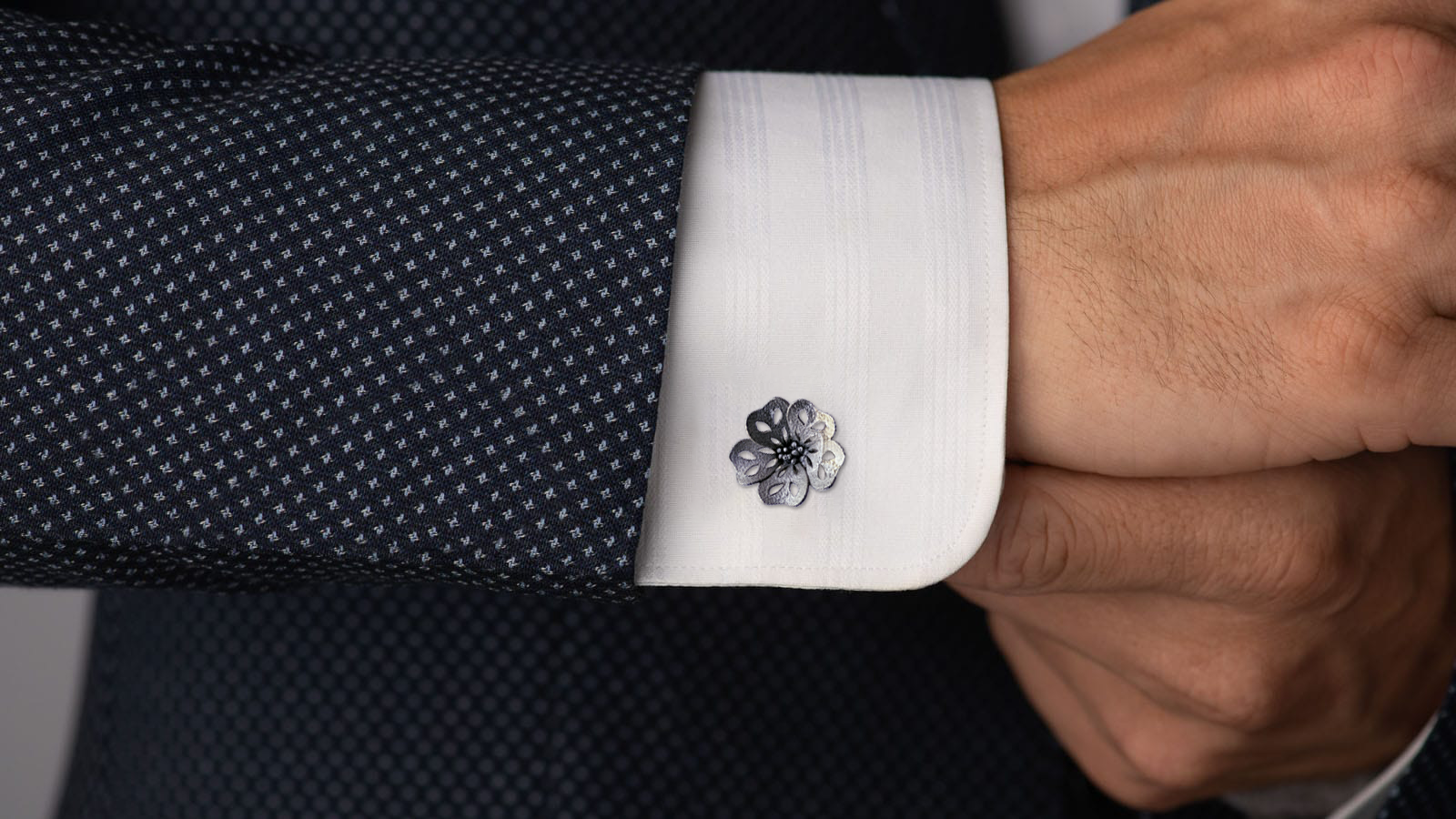 Open-flower cufflink worn on a white shirt cuff beneath a dark jacket