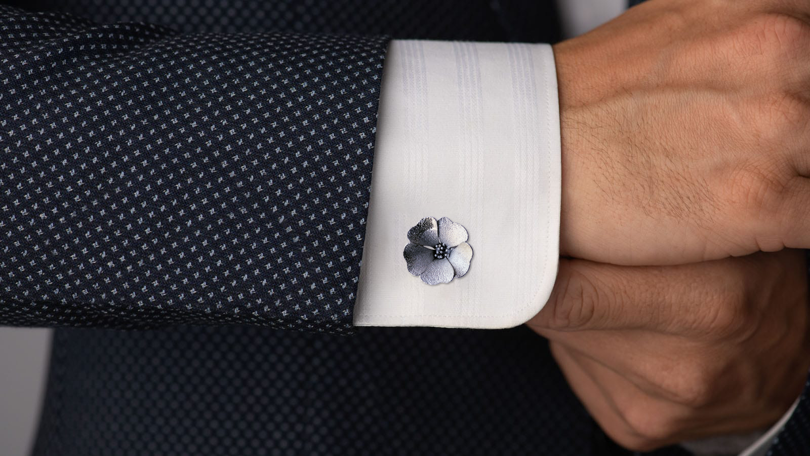 Solid-flower cufflink worn on a white shirt cuff beneath a dark jacket