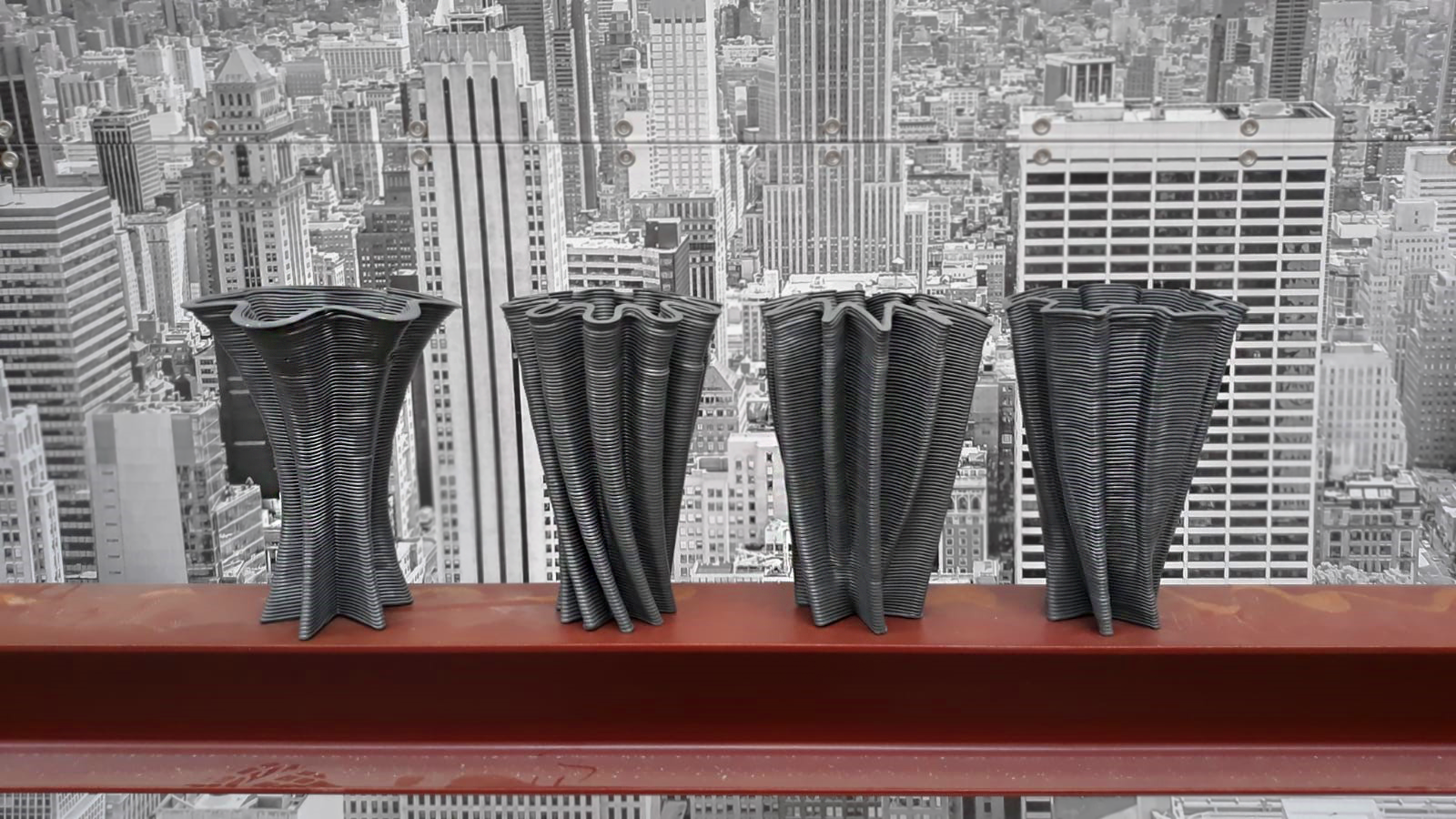 Four finished, ribbed parametric vases displayed on a red ledge against a cityscape