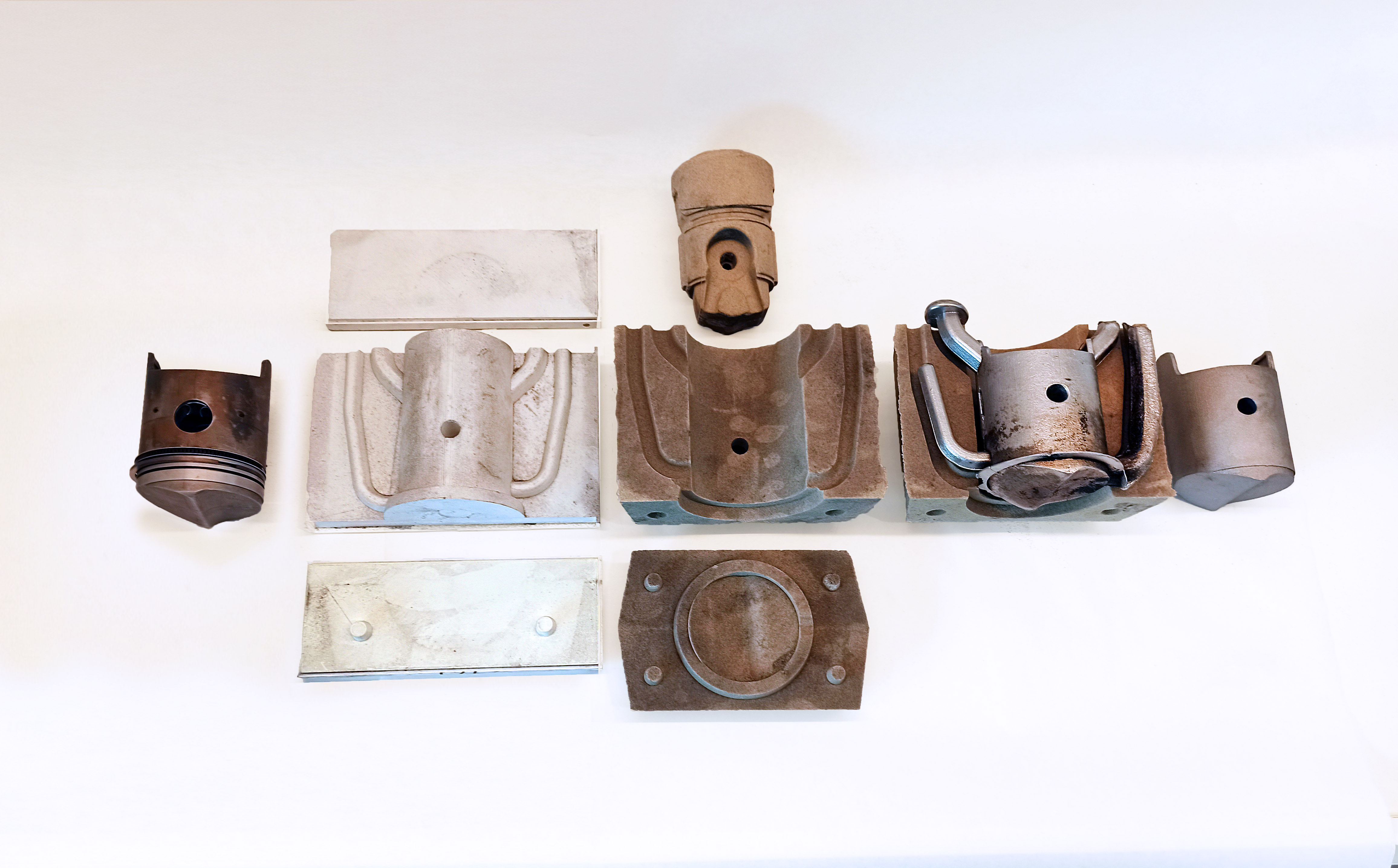 Original piston, mould patterns, sand moulds, casting, and trimmed replacement arranged as a production sequence